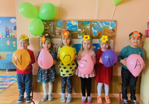 Dzieci pozują do zdjęcia z balonikami podpisanymi „wiosna”