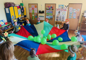 Dzieci bawią się chustą animacyjną podrzucając zielone balony