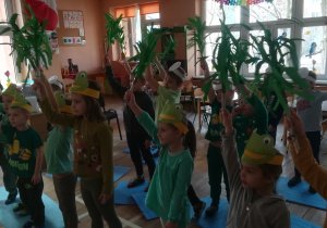 Dzieci z zielonymi miotełkami w ręku uczą się układu tanecznego