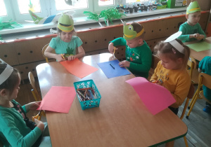 Dzieci siedzą przy stoliku i wycinają elementy z kolorowych kartek
