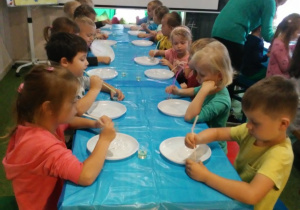 Dzieci siedzą przy stoliku na którym są plastikowe talerze