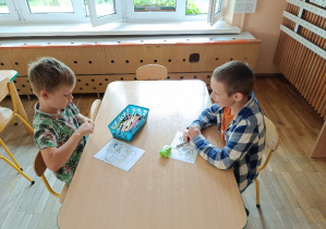 Chłopcy siedzą przy stoliku i kolorują kredkami obrazki