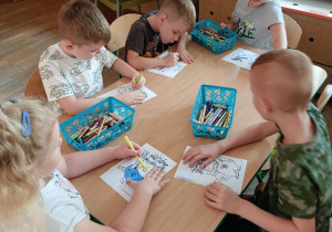Dzieci siedzą przy stoliku i kolorują kredkami obrazki
