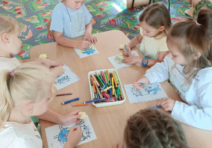 Dziewczynki siedzą przy stoliku i kolorują kredkami obrazki
