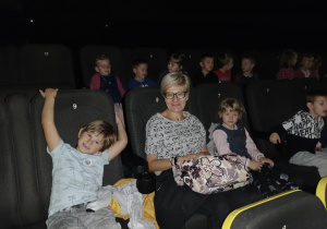 Dzieci z panią siedzą na fotelach w kinie