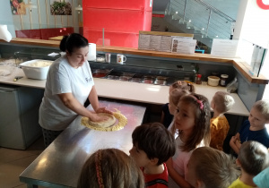 Pracownica Pizzerii pokazuje dzieciom jak należy rozkręcać ciasto na pizzę.