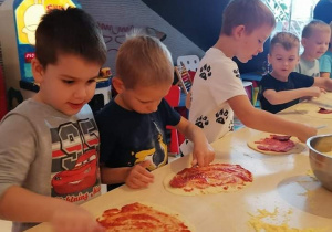 Dzieci smarują pizzę sosem i układają dodatki.