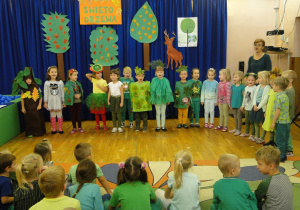 Dzieci przebrane za drzewa śpiewają piosenkę.
