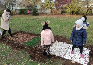 Dzieci i pani dyrektor spacerują w ogrodzie po ścieżce sensorycznej