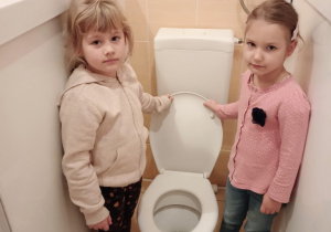 Dwie dziewczynki pokazują opuszczanie klapy w toalecie
