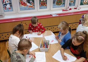 Dzieci przy stolikach siedzą i kolorują obrazki