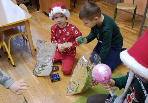 Dzieci siedzą na dywanie - otwierają prezenty od Mikołaja