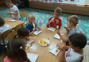 Dzieci jedzą owocowe szaszłyki.