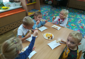 Dzieci jedzą owocowe szaszłyki.