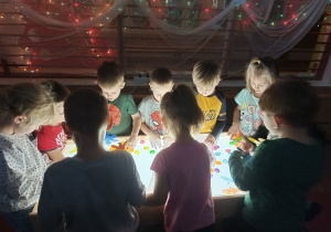 Dzieci bawią się kolorowymi przedmiotami na podświetlanym stole sensorycznym