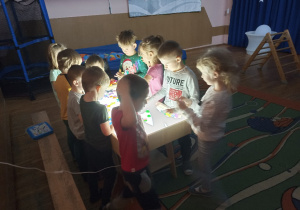 Dzieci bawią się kolorowymi przedmiotami na podświetlanym stole sensorycznym