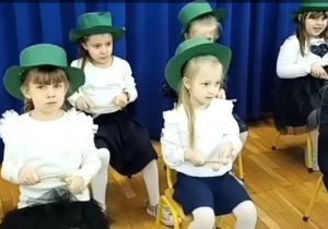 Dzieci siedzą na krzesełkach w zielonych kapeluszach