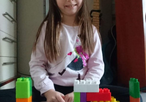 Dziewczynka prezentuje skonstruowaną przez siebie budowlę z klocków lego duplo.