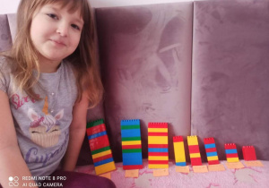 Dziewczynka prezentuje wieże zbudowane z tylu klocków ile wskazuje cyfra na kartce.