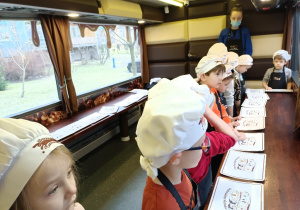 Dzieci w czapkach kucharskich słuchają informacji o czekoladzie