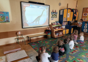 Dzieci oglądają film o dinozaurach na dużym ekranie.