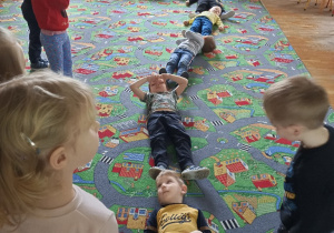 Pięciu chłopców jeden za drugim leżą na dywanie ukazując jak daleko mogą polecieć bakterie przy kichaniu