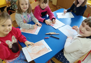 Dzieci przy stolikach kolorują obrazki.
