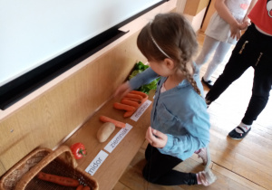 Dziewczynka odczytuje i dopasowuje napisy do zgromadzonych warzyw.