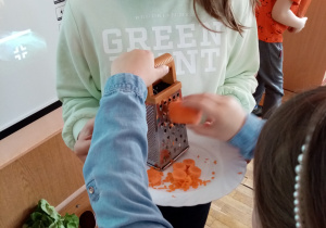 Dziewczynki ścierają marchewkę na tarce.
