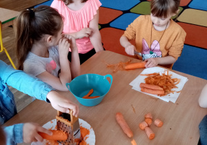 Dzieci obierają marchewki i ścierają je na tarce.
