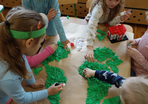 Dziewczynki wyklejają zieloną bibułą kontury kontynentów