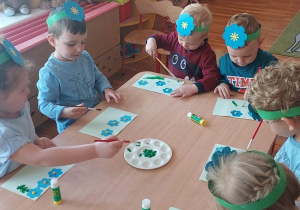Dzieci układają i naklejają kompozycje kwiatków w niebieskich kolorach