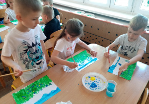 Dzieci malują farbami plakatowymi łąkę z niezapominajkami.