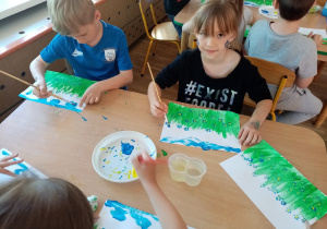 Dzieci malują farbami łąkę z niezapominajkami.