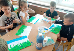 Dzieci malują farbami łąkę z niezapominajkami.