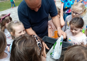 Pan Rafał pomaga dzieciom sypać ziemi do doniczki.