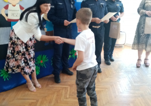 Mateusz odbiera dyplom i nagrodę z rąk policjanta.