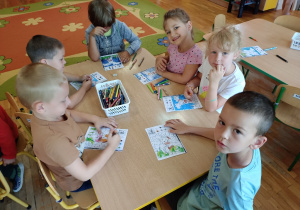 Dzieci siedząc przy stoliku kolorują obrazki.