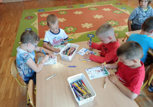 Dzieci siedząc przy stoliku kolorują obrazki.