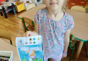 Dziewczynka pokazuje swój pokolorowany obrazek.
