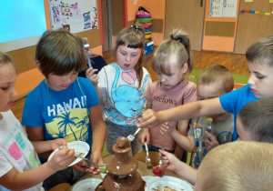 Dzieci jedzą różne smakołyki maczane w fontannie czekoladowej.