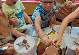 Dzieci jedzą różne smakołyki maczane w fontannie czekoladowej.