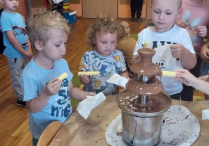 Dzieci jedzą pałeczki kukurydziane maczane w czekoladowej fontannie