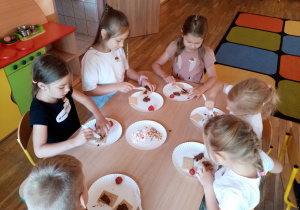 Dziewczynki dekorują herbatniki czekoladą, truskawkami i posypkami.
