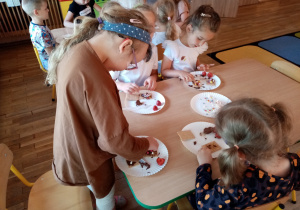 Dziewczynki dekorują herbatniki czekoladą, truskawkami i posypkami.