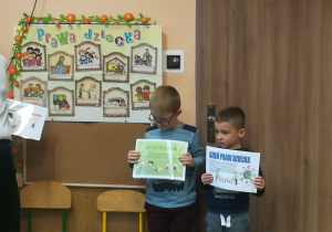 Na tablicy przypięte są prawa dziecka w obrazkach, dwoje dzieci obok trzyma kartki z informacjami o tym dniu