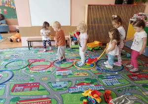 Przedszkolaki skaczą na dywanie do obręczy.