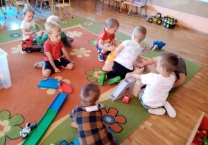 Dzieci bawią się na dywanie torami samochodowymi.