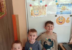 Trzech chłopców na tle tablicy z obrazkami o uśmiechu