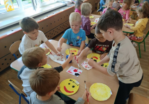 Dzieci przy stoliku malują farbami buźki z uśmiechem